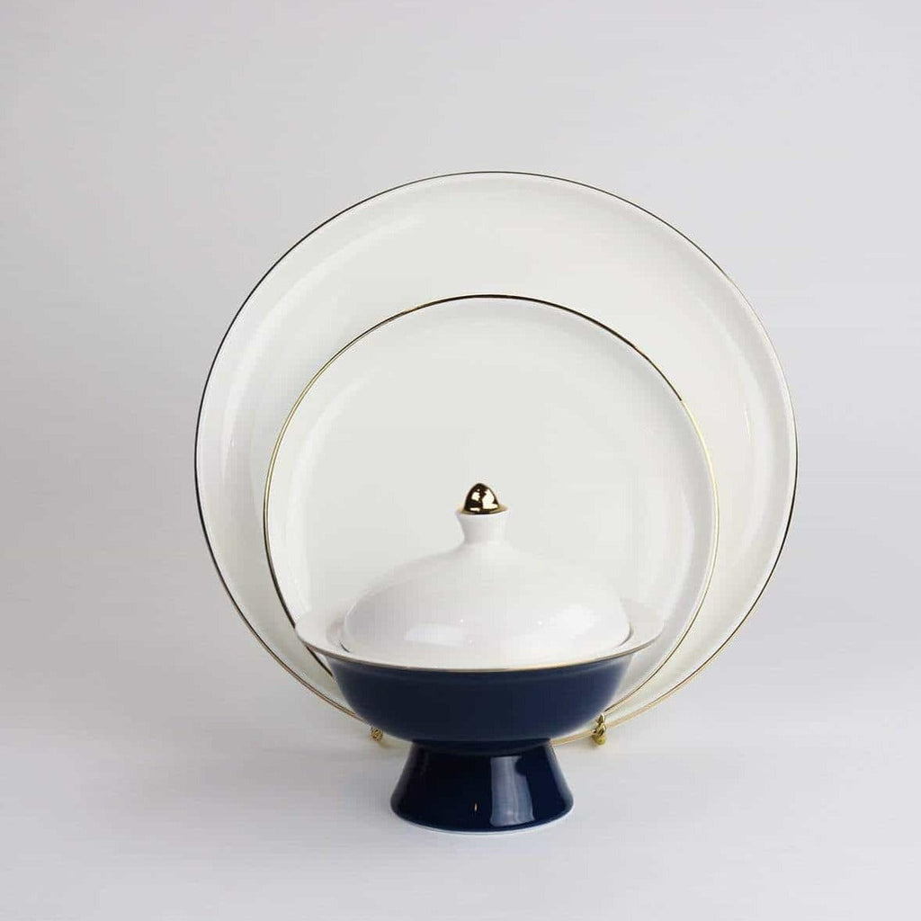 Elegant white dinnerware set with gold trim and navy blue bowl on plain background