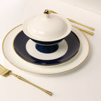 Elegant navy and white dinnerware set with gold rim, matching covered bowl, and gold cutlery