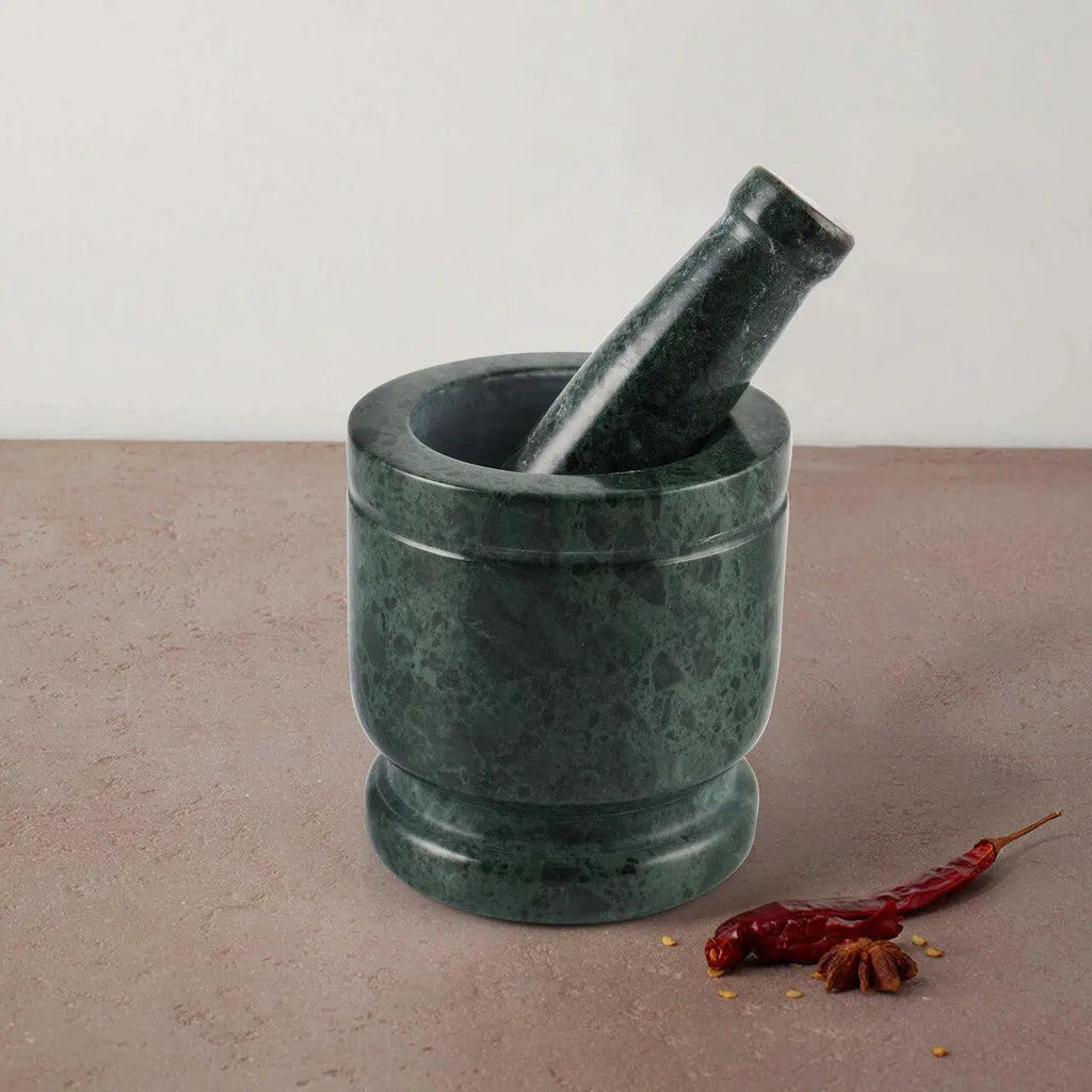 Green marble mortar and pestle on a beige surface with dried red chili peppers.