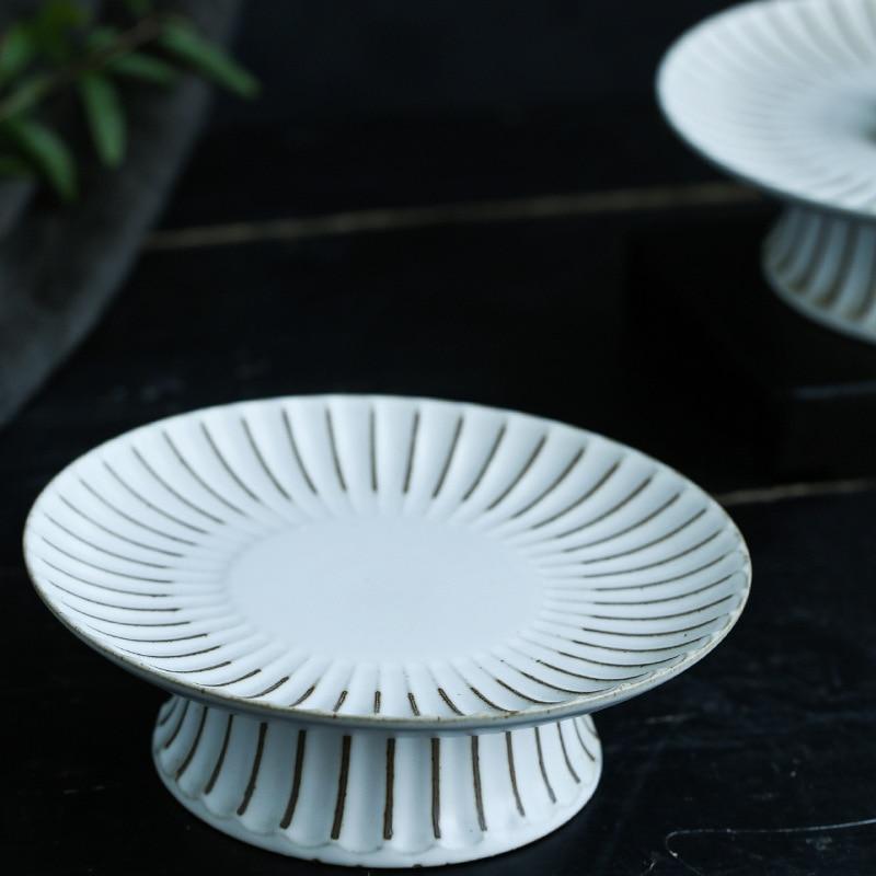 White ceramic pedestal plate on a dark surface with blurred greenery in the background