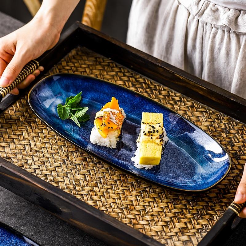 Eye of Ocean ceramic long plate — served with sushi on rattan tray, deep blue iridescent glaze with gold-fired rim
