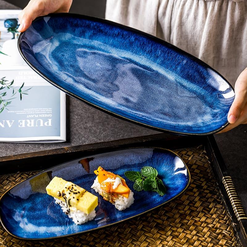Large and medium Eye of Ocean ceramic oval plates — both sizes shown side by side, cobalt blue reactive glaze with gold rim
