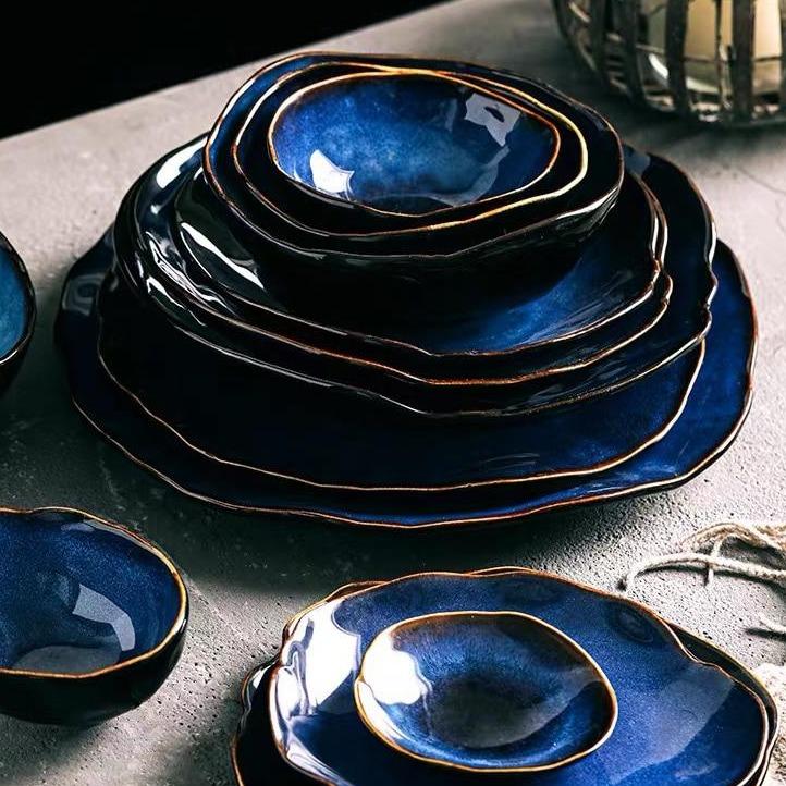 Amelia Blue Porcelain Dinnerware Set — full 18-piece collection laid out on a dark surface with cobalt blue reactive glaze and bronze rim detail
