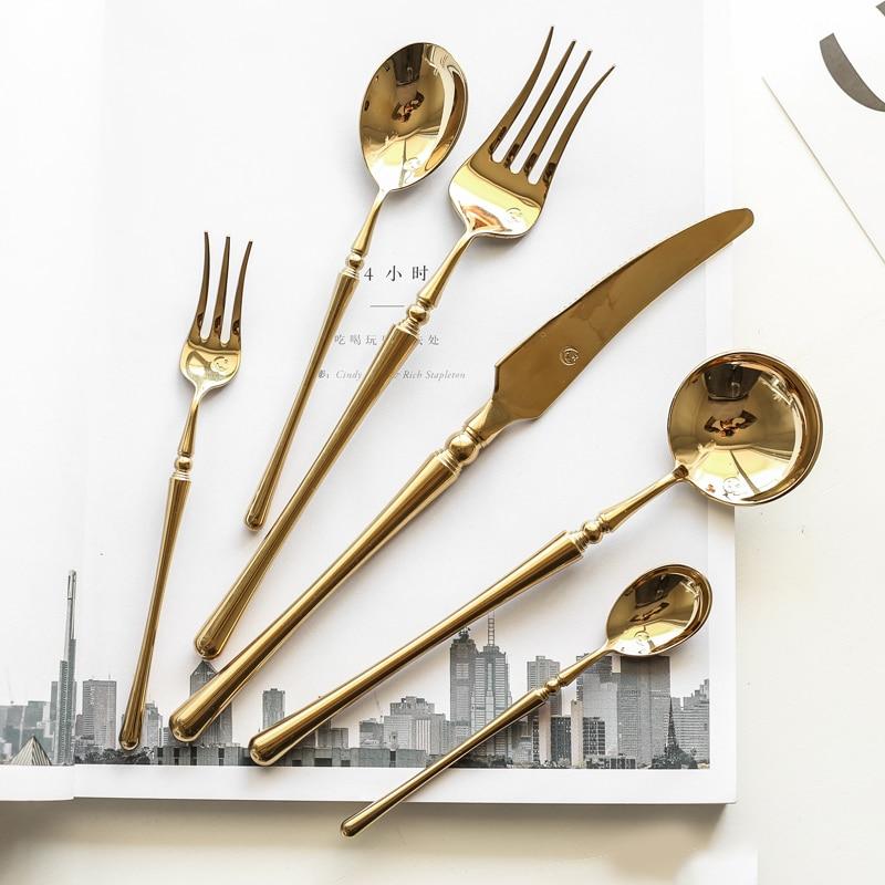 Set of gold-colored cutlery including a knife, fork, and two spoons on a magazine with a cityscape background.