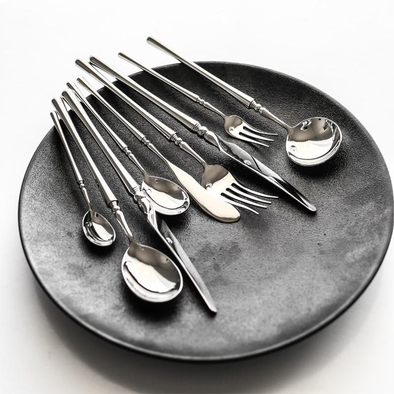 Set of silver cutlery including forks, knives, and spoons on a dark gray plate.