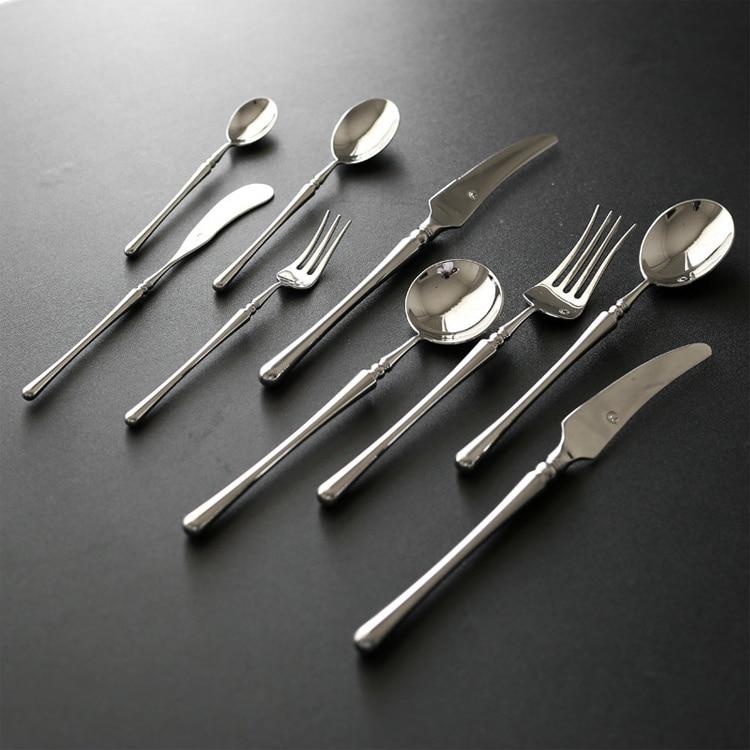Set of silver cutlery including knives, forks, and spoons on a dark surface