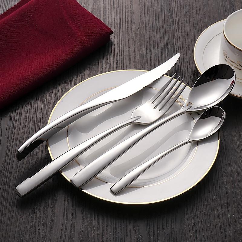 Silver cutlery set on a white plate with a red napkin and cup in the background.