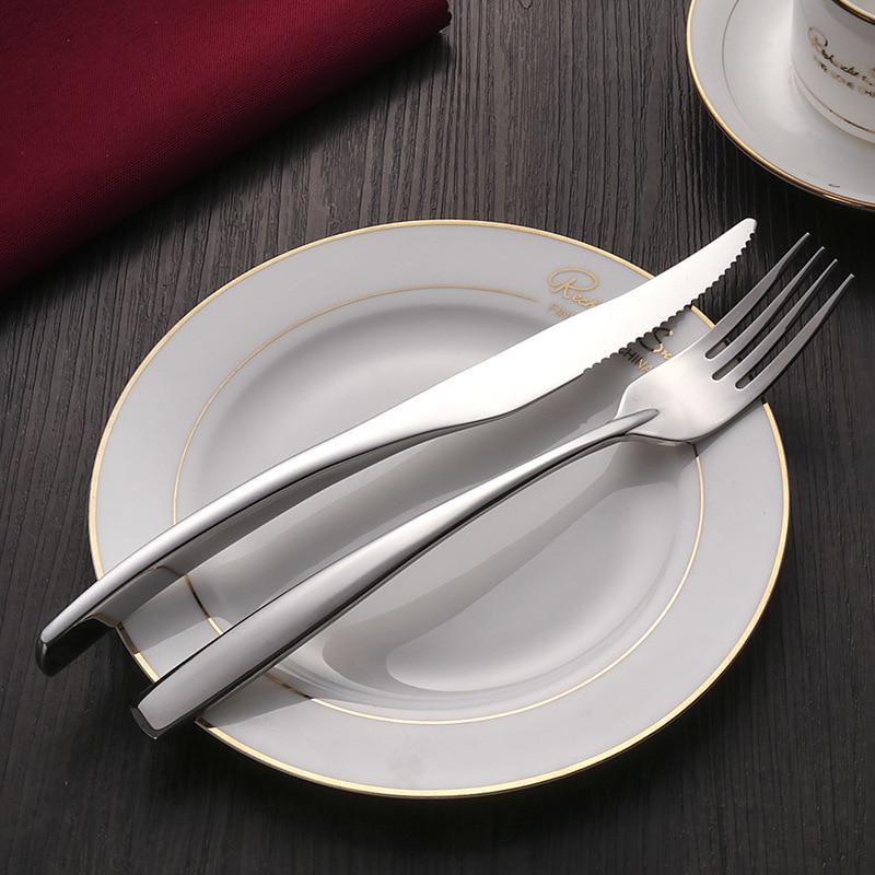 Silver cutlery set on a white plate with a red napkin and cup in the background.