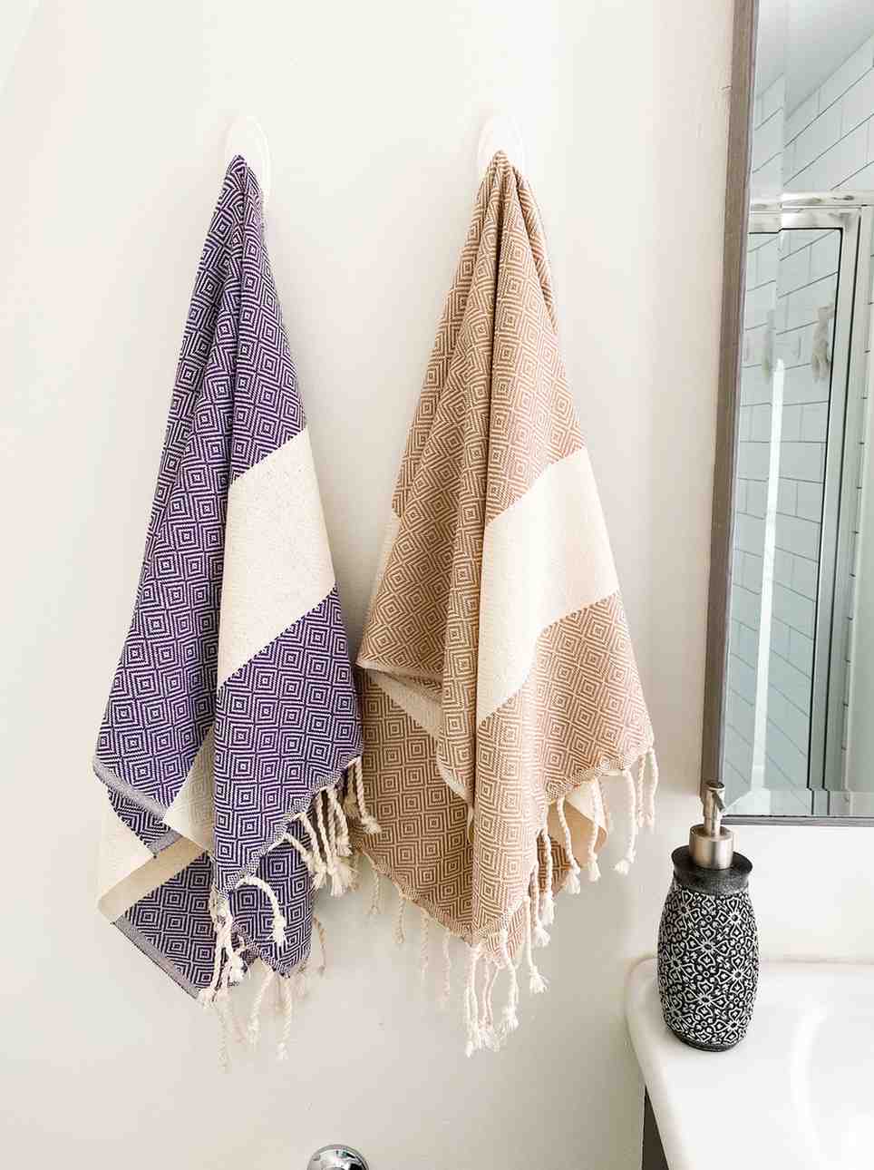 Purple and beige diamond-patterned hand towels with fringe hanging in a modern bathroom
