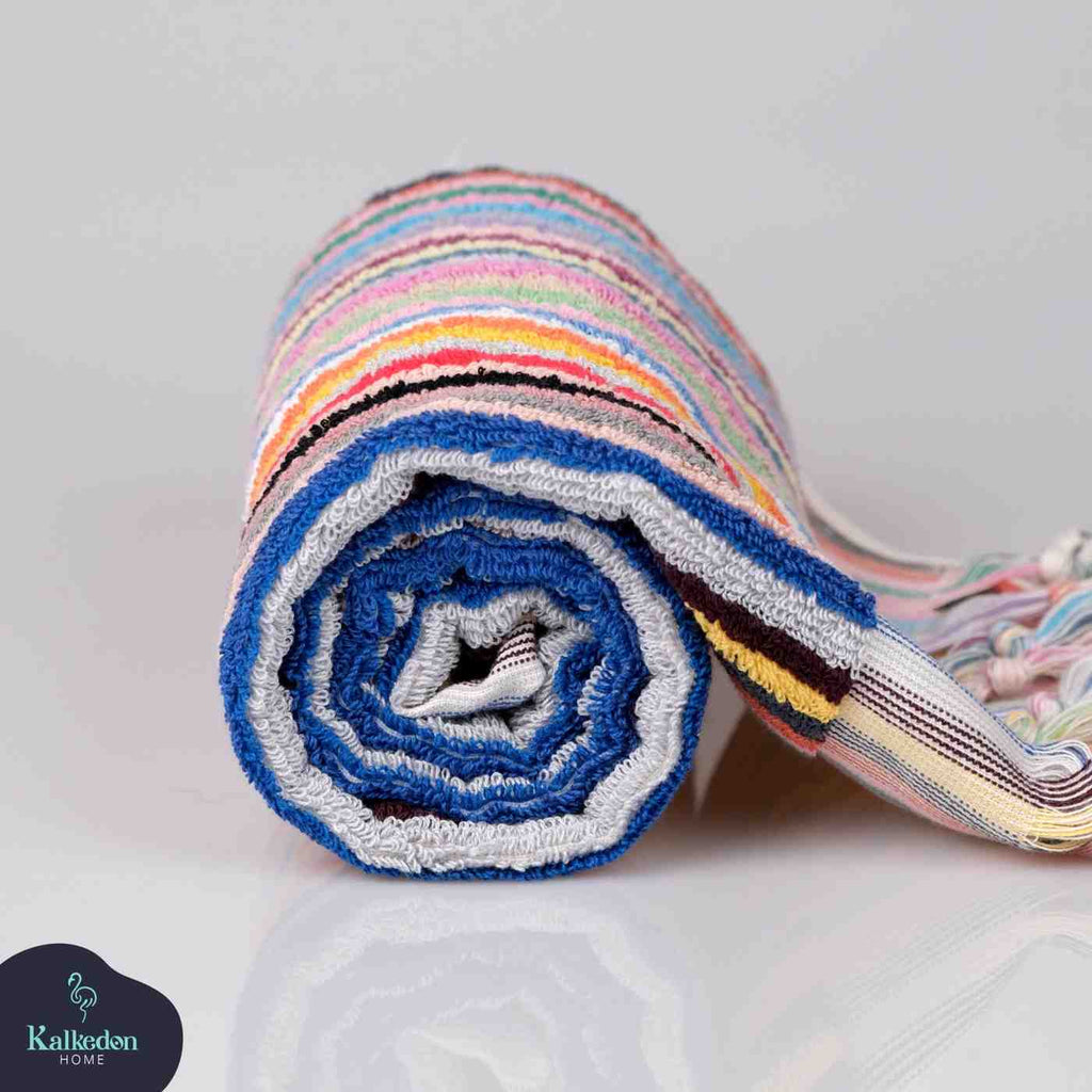 Folded rainbow striped hand towel with colorful fringe on white background