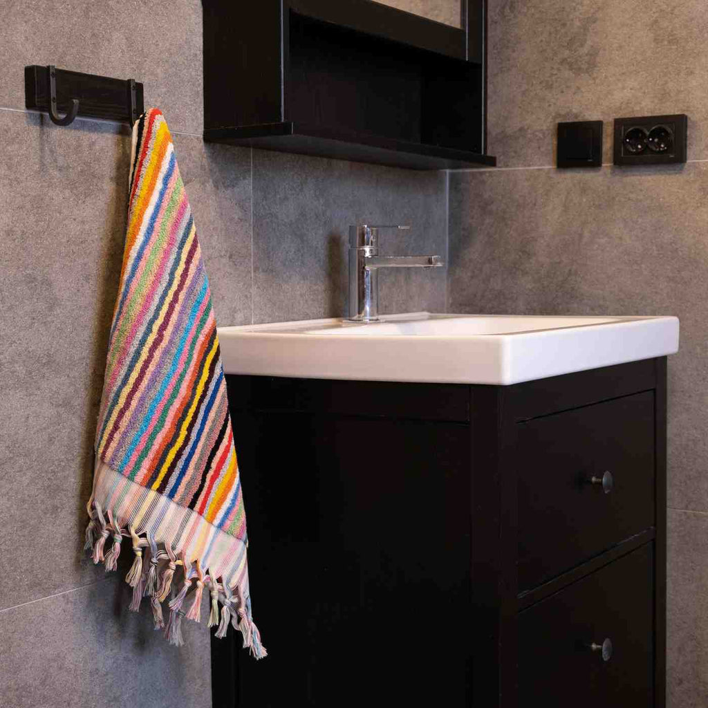 Rainbow striped hand towel with tassels hanging by a modern bathroom sink