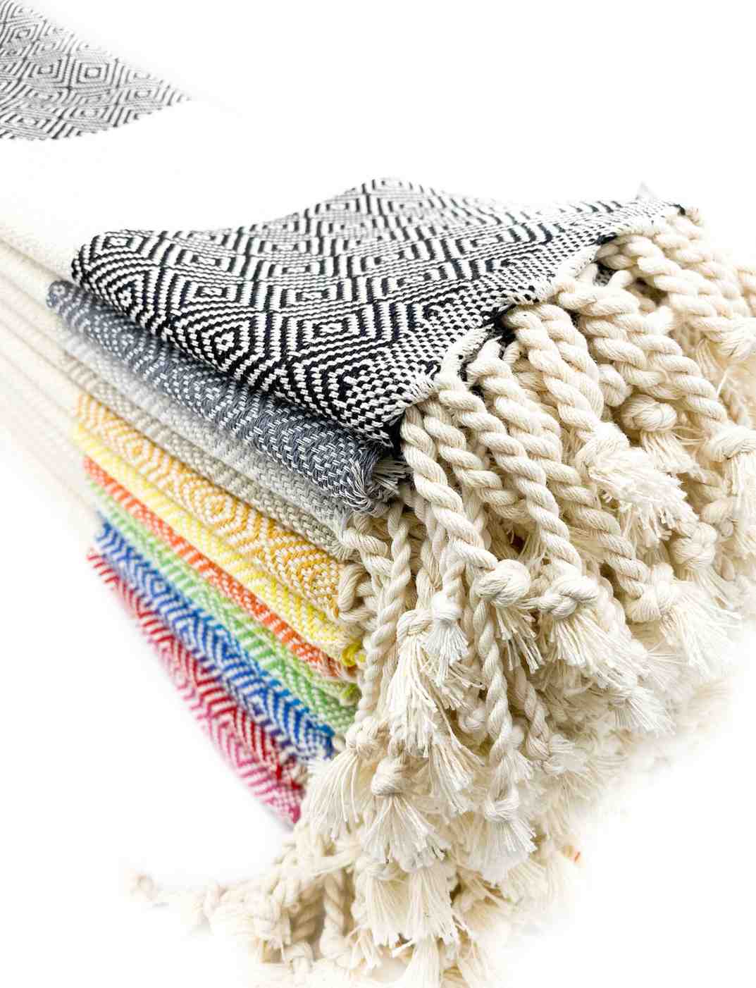 Stack of assorted Turkish hand towels in colorful patterns with twisted fringe edges