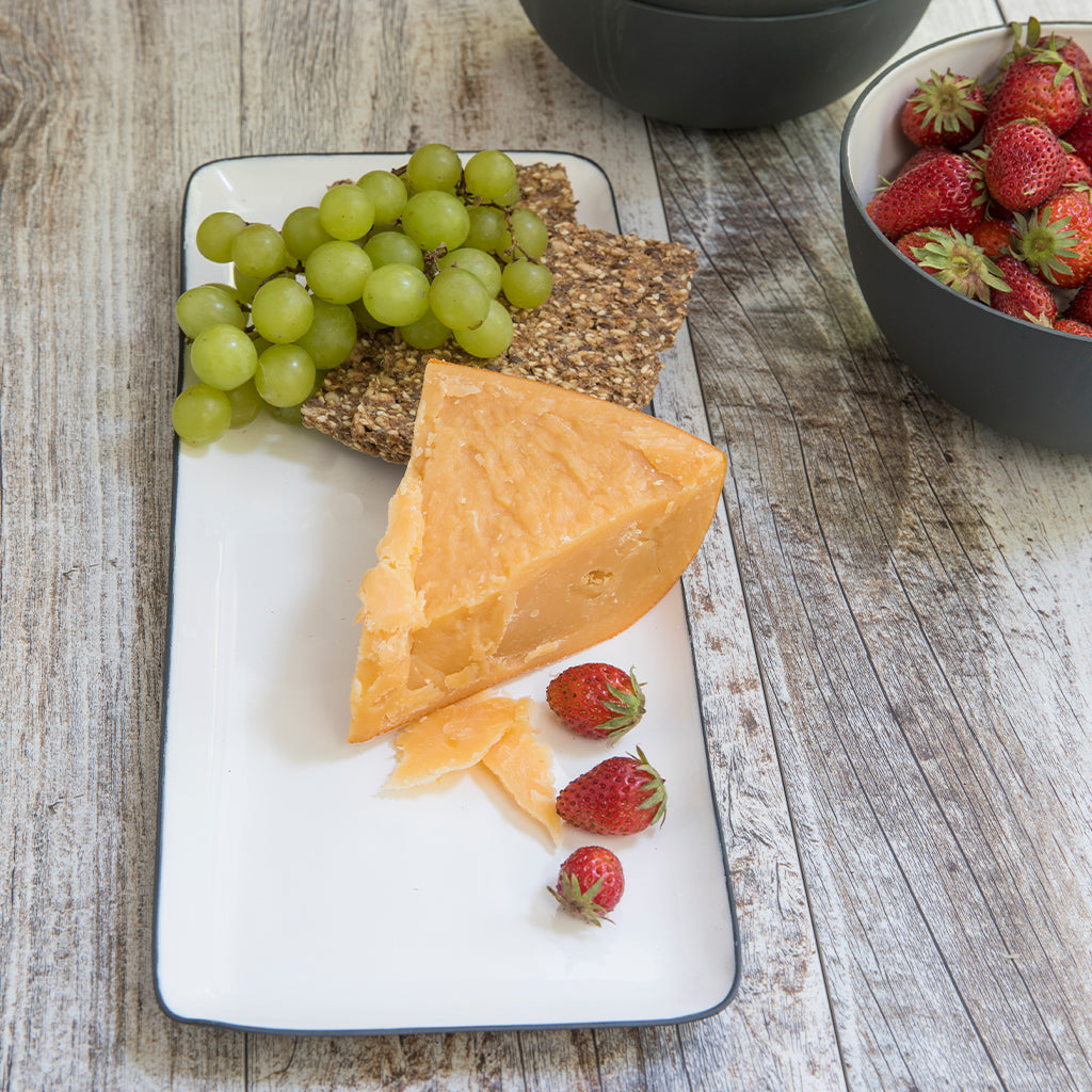 Platter of cheese, crackers, and grapes on a wooden table with strawberries.