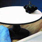 Black grapes on a white round cake stand with a blue background