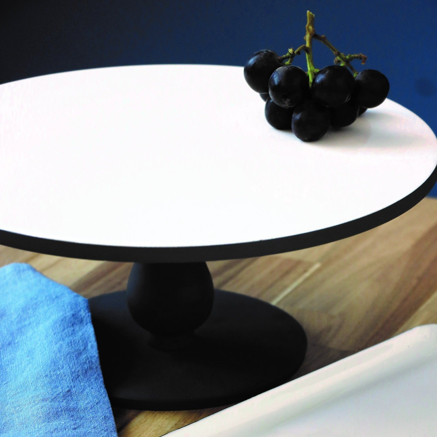 Black grapes on a white round cake stand with a blue background