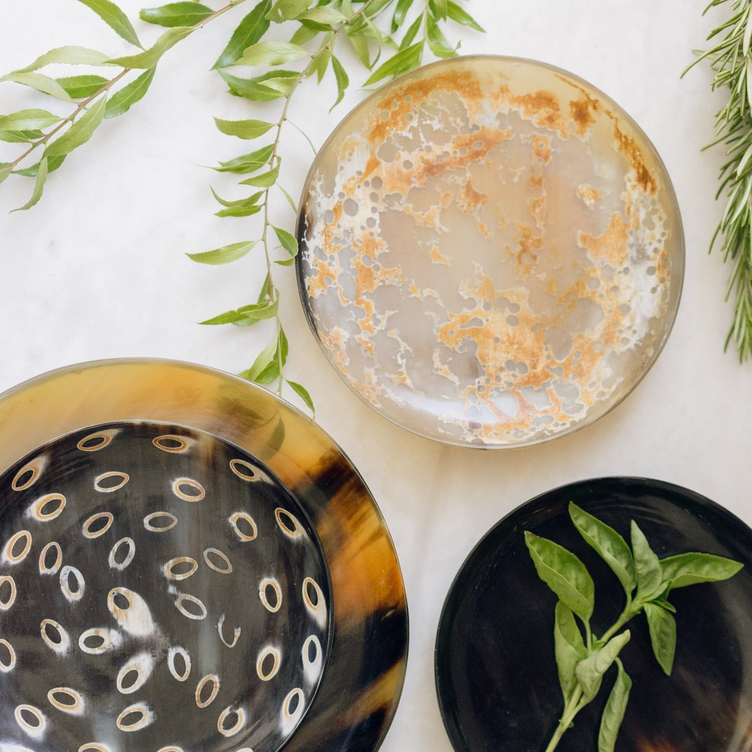 Three decorative plates with unique patterns on a light background with greenery.