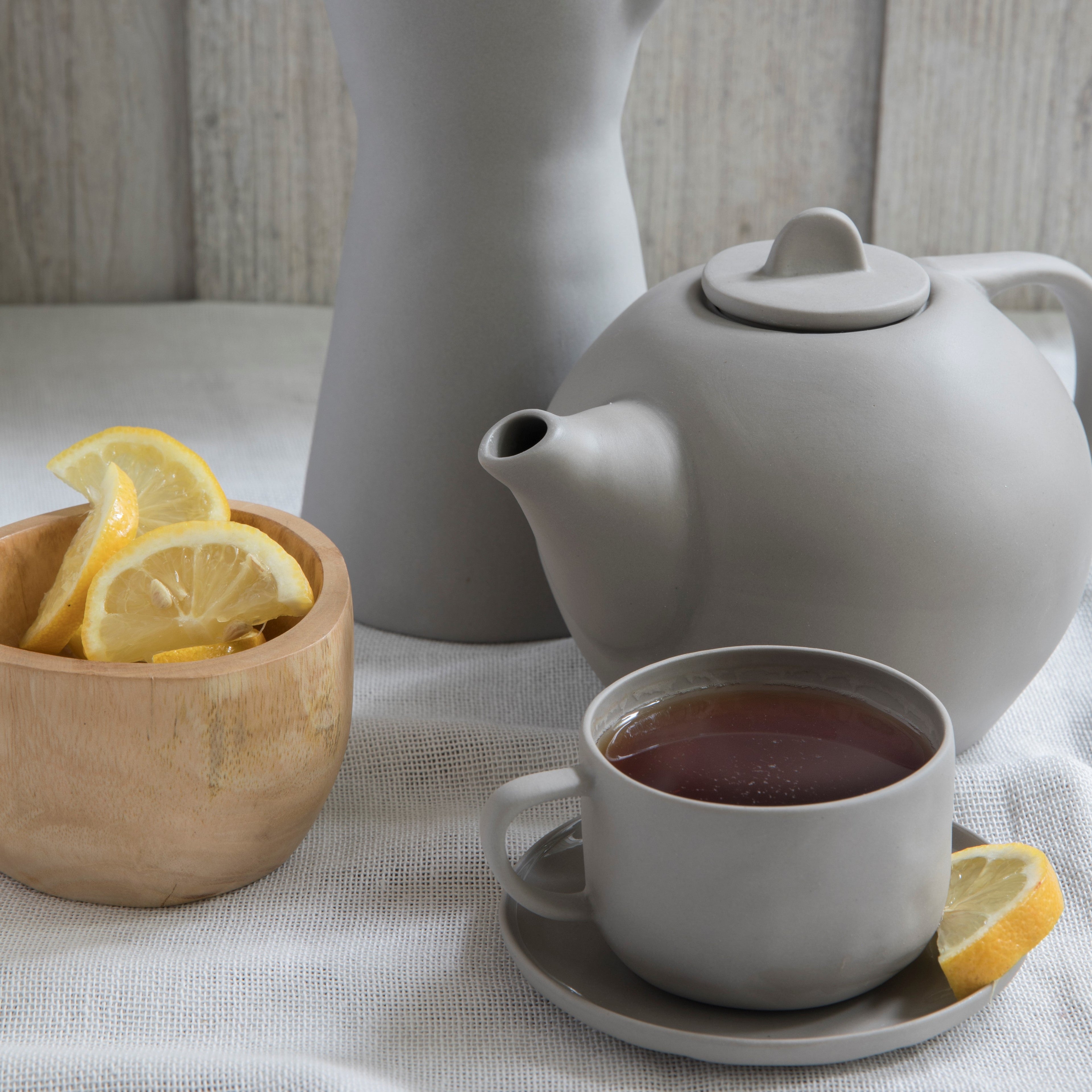 White teapot and cup with lemon slices on a light surface