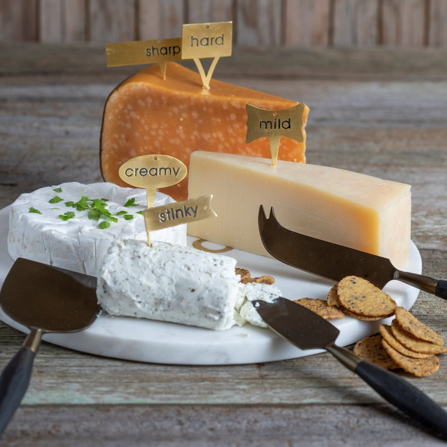 Assorted cheeses on a platter with labels and crackers on a wooden surface
