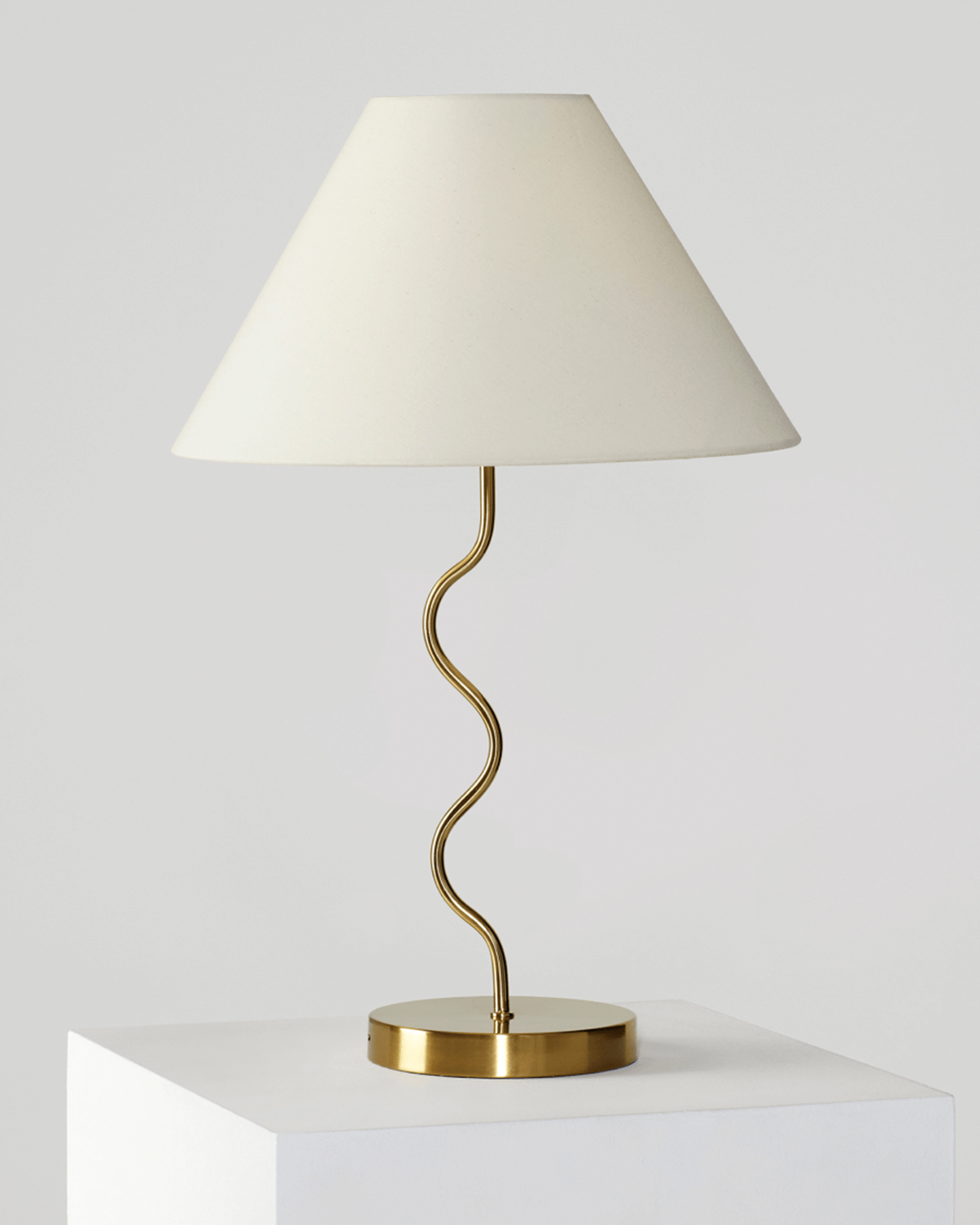 Table lamp with a white shade and gold curved base on a white surface.
