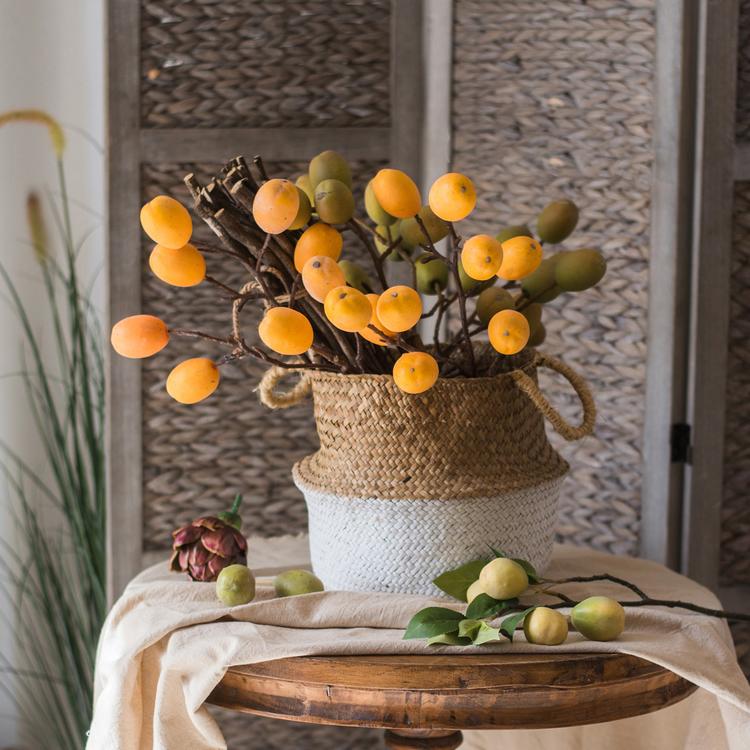 Decorative arrangement with orange fruits in a woven basket on a wooden stool.