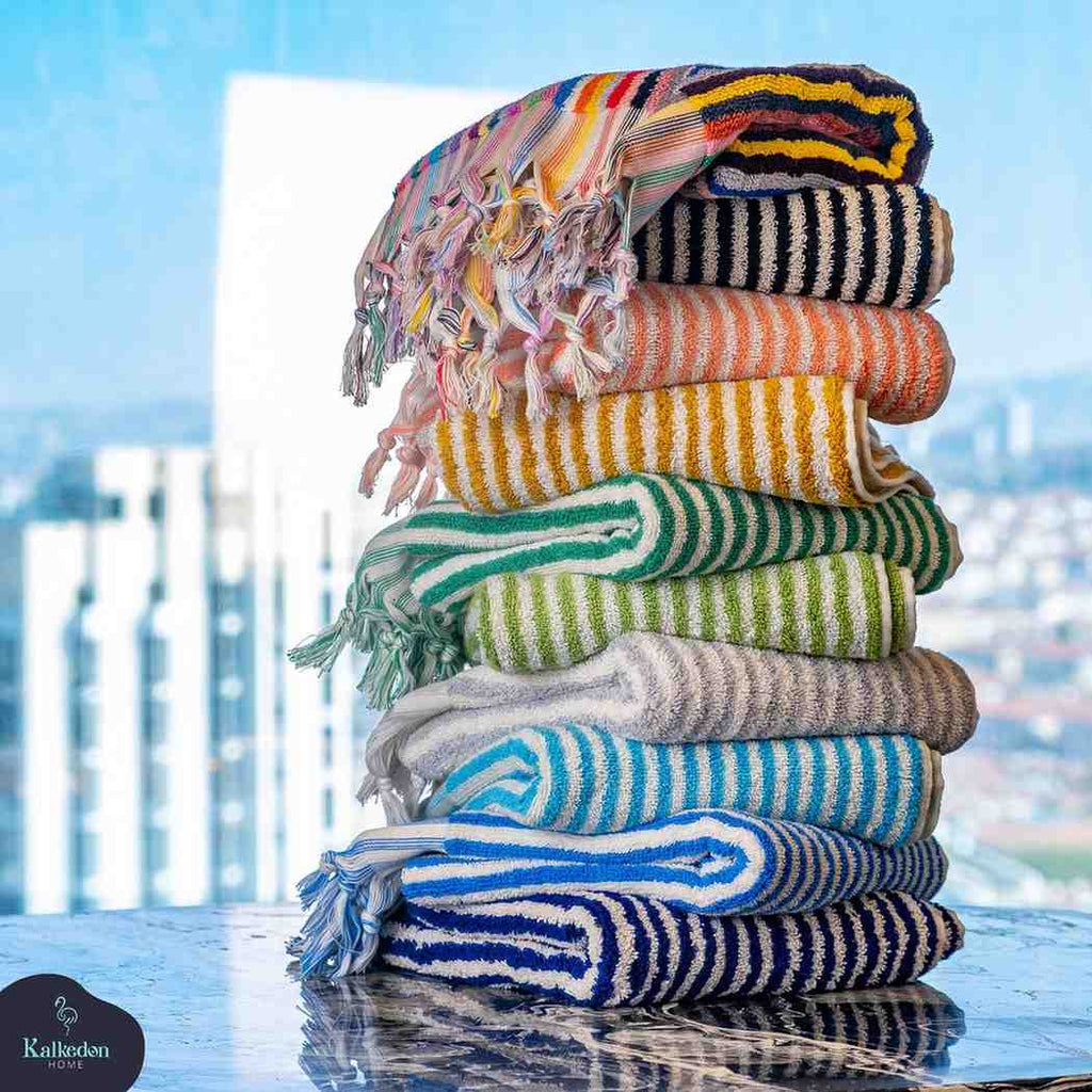 Stack of colorful striped jacquard hand towels with fringe on marble surface