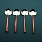 Four heart shaped spoons with copper handles on a dark green background