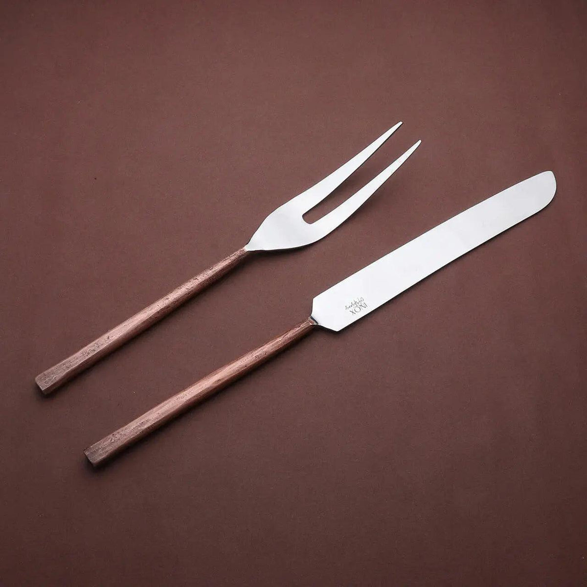 Sundance meat carving knife and two-tined fork with textured copper-toned handles, angled together on a brown background.