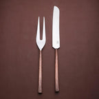 Sundance meat carving knife and two-tined fork with textured copper-toned handles, angled together on a brown background.