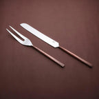 Sundance meat carving knife and two-tined fork with textured copper-toned handles, angled together on a brown background.