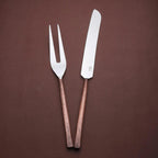 Sundance meat carving knife and two-tined fork with textured copper-toned handles, angled together on a brown background.