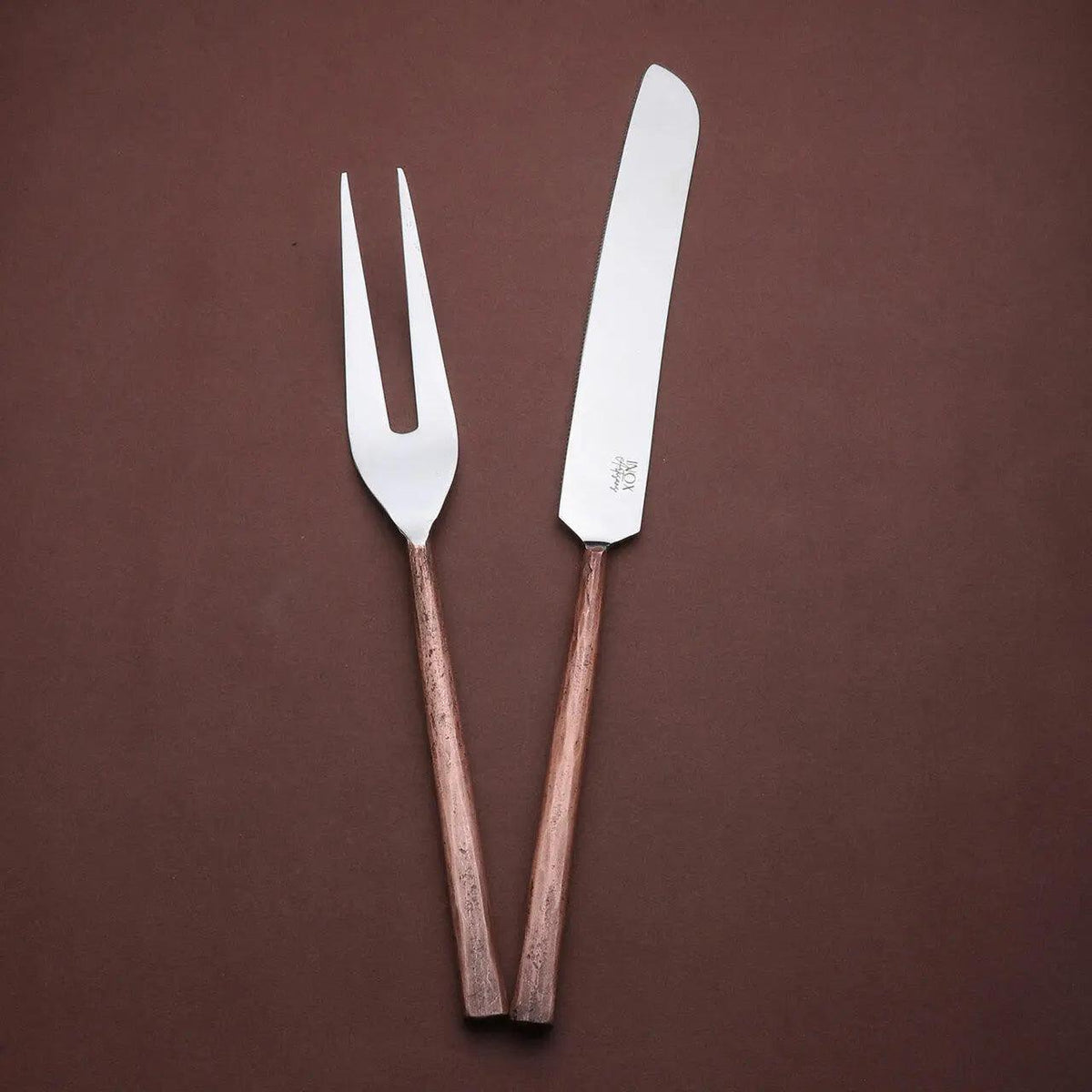 Sundance meat carving knife and two-tined fork with textured copper-toned handles, angled together on a brown background.