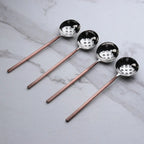 Set of four copper ladles with holes with black handles on a marble surface