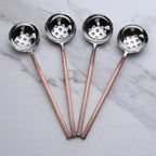 Four metal ladles with copper handles on a marble surface