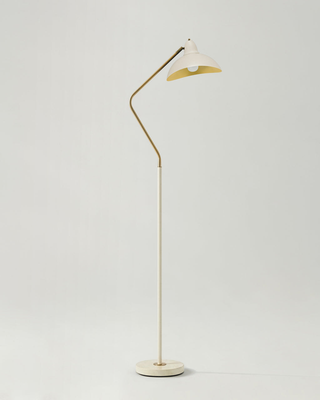 Floor lamp with a white shade and gold metal arm on a light gray background