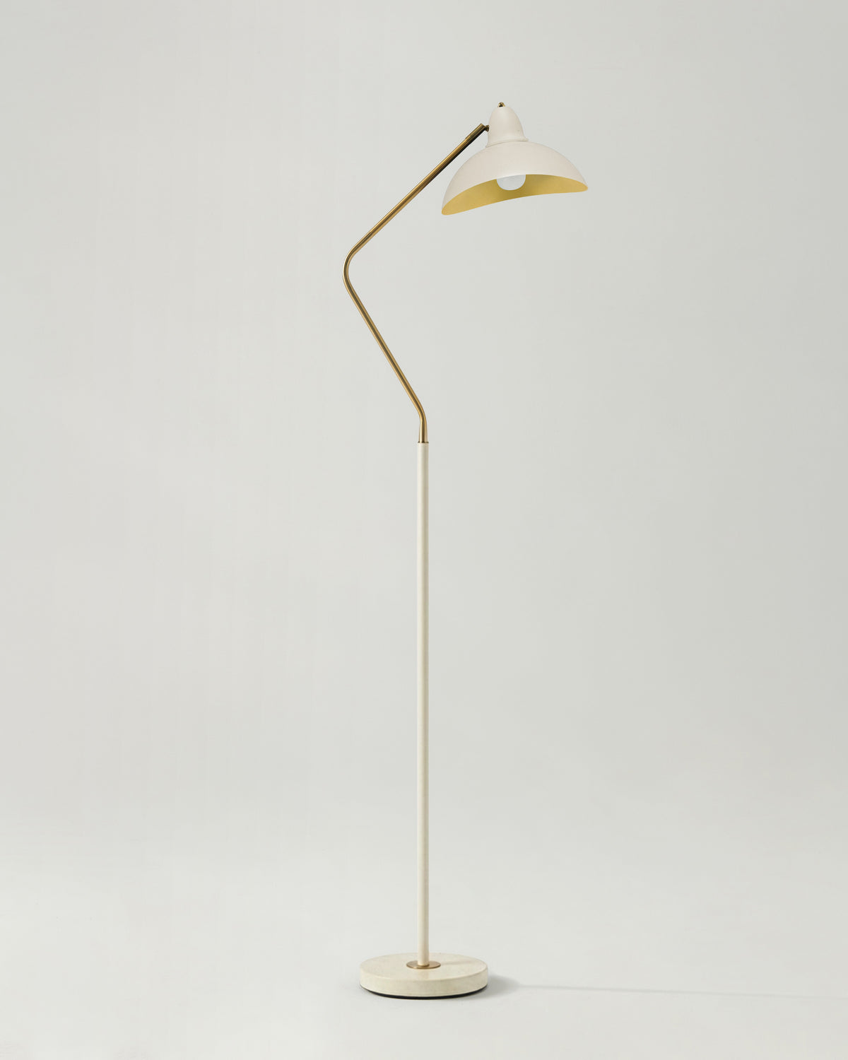 Floor lamp with a white shade and gold metal arm on a light gray background