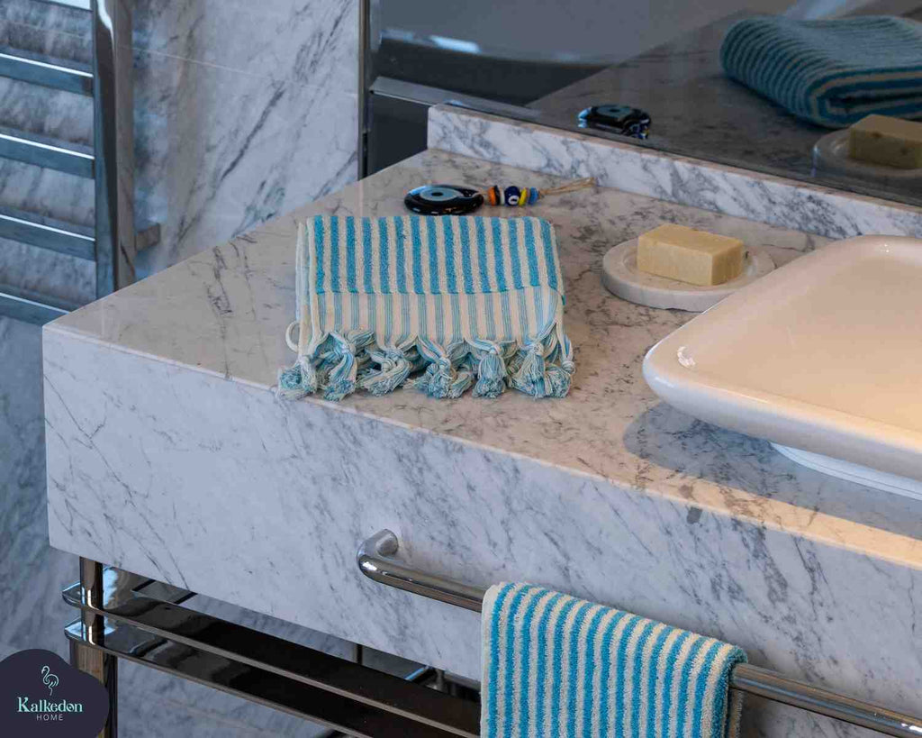 Turquoise striped hand towel with tassels on marble bathroom counter near soap dish