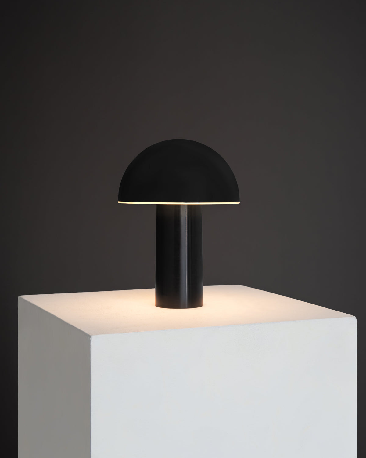 Black table lamp on a white pedestal against a dark background