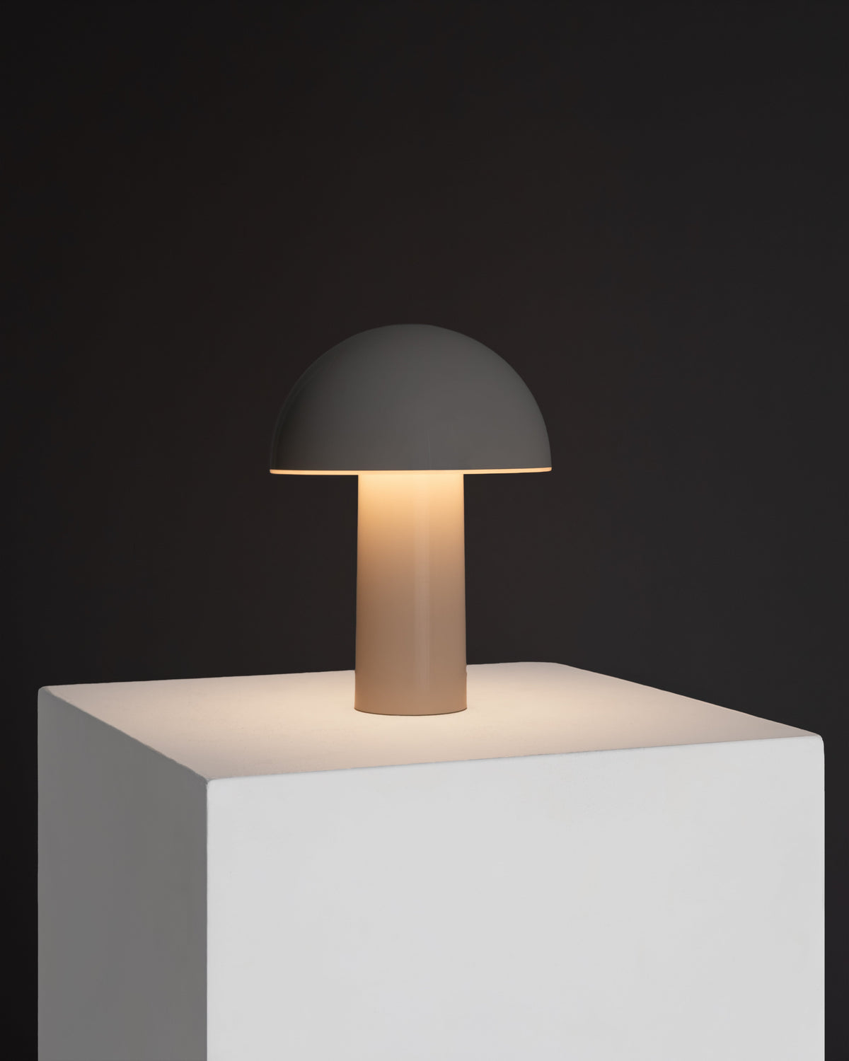 Modern table lamp with a dark gray shade and base on a white pedestal against a black background.