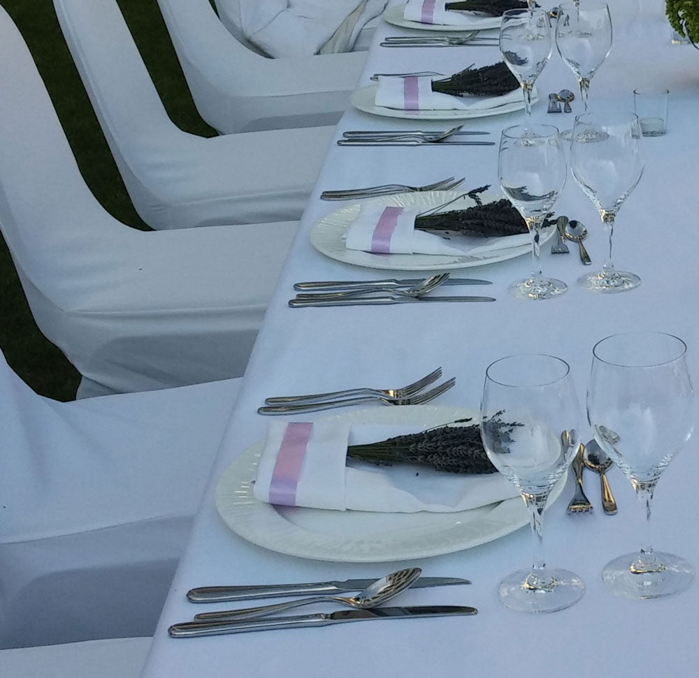 Elegant table setting with white tablecloth, silverware, and wine glasses on a white chair background.