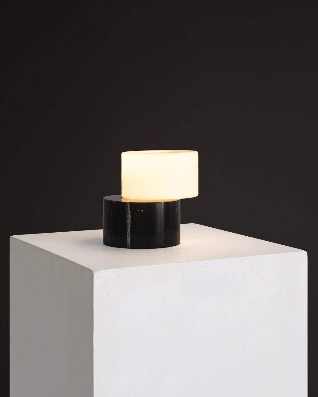Small lamp with a black base and white shade on a white pedestal against a dark background