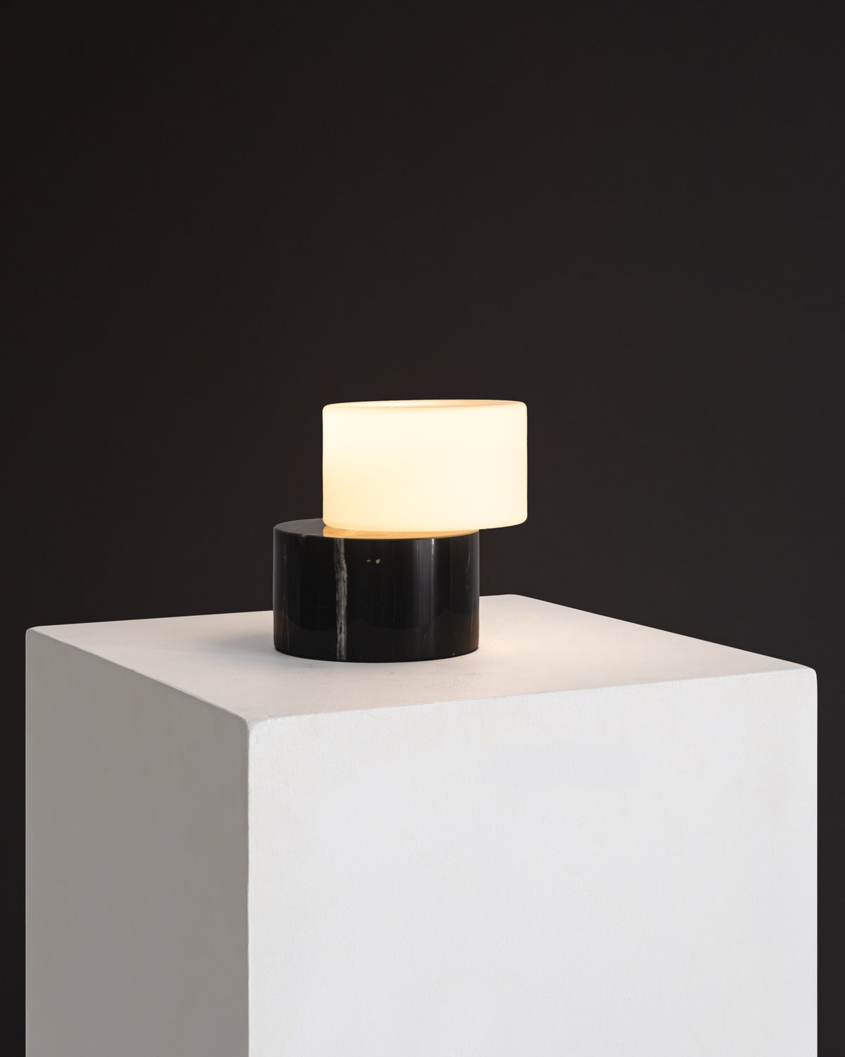 Small lamp with a black base and white shade on a white pedestal against a dark background